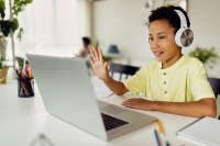 Smiling black boy making video call over laptop and waving while e-learning at home. 