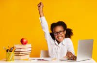 Black Elementary Student Girl Raising Hand Sitting At Laptop Doing Homework Over Yellow Background. Studio Shot